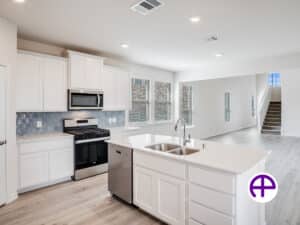 Elegant kitchen featuring white cabinets, white quartz countertops, island with double sink, and tiled backsplash