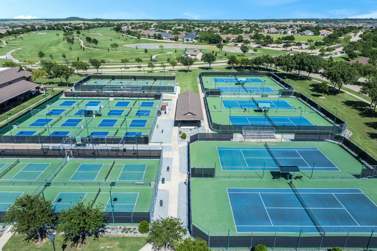 Aerial Drone Photography Of Sports And Recreational Amenities In Dallas, Texas Aerial drone photography of outdoor tennis and pickleball courts surrounded by green spaces at a residential community in dallas, texas.