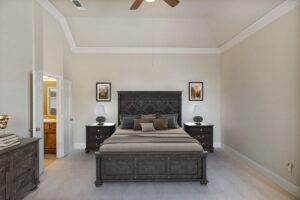 Digitally staged primary bedroom featuring modern dark wood furniture, vaulted ceilings, and tasteful decor for a rental property listing.